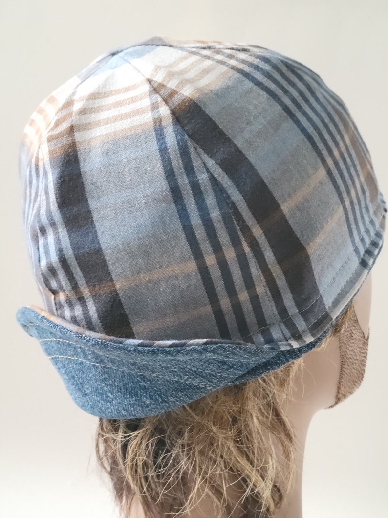 May include: A brimless cap featuring a plaid pattern in shades of blue, grey, and tan. The hat has a structured crown with a folded, denim-textured blue band around the base, showcasing visible stitching along the edge of the folded fabric.