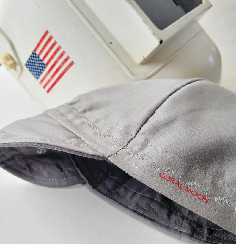 Pu&ograve; includere: Un cappello da baseball grigio con visiera nera e il testo "CORAL MOON" ricamato in rosso sul lato.