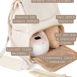 May include: A cream-colored vegan leather diaper bag with gold hardware. The bag has a large pocket on the front, two zippered pockets on the side, and a padded laptop compartment. It also includes a wet/dry bag and stroller straps.  The bag is open to reveal a breast pump inside.