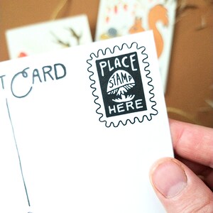 May include: A white postcard with black ink. The postcard says "PLACE STAMP HERE" with a mushroom graphic. The postcard also says "POSTCARD" in the top left corner.