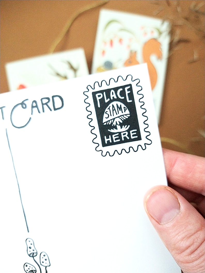 May include: A white postcard with black ink. The postcard says "PLACE STAMP HERE" with a mushroom graphic. The postcard also says "POSTCARD" in the top left corner.