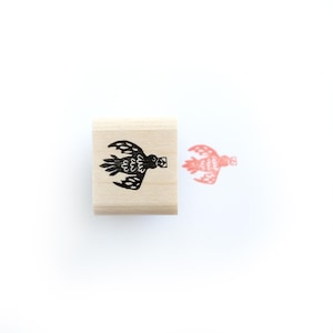May include: A wooden stamp with a black silhouette of a bird with wings spread. The stamp is on a white background and there is a red ink impression of the bird to the right of the stamp.