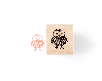 May include: A wooden stamp with a black and white illustration of an owl. The owl has large eyes and a round body. The stamp is on a white background.