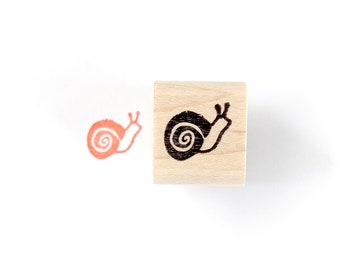 May include: A wooden stamp with a black snail design. The stamp is used to create a red snail impression.