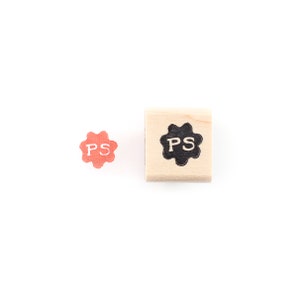 May include: Two wooden stamps with a starburst design. The stamp on the left is red and says "PS" in white. The stamp on the right is black and says "PS" in white.