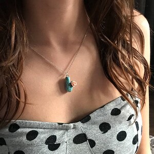 May include: A woman wearing a black and white polka dot top with a silver chain necklace featuring a turquoise and rose gold pendant.