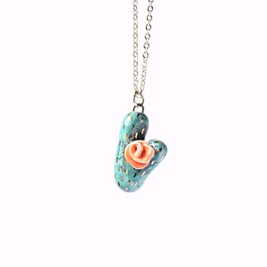May include: A turquoise ceramic cactus necklace with a pink flower on top. The necklace has a silver chain.