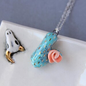 May include: A turquoise ceramic cactus pendant with gold accents and a pink ceramic flower, hanging from a silver chain.