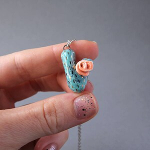 May include: A turquoise and gold cactus pendant necklace with a pink flower on top. The necklace is on a silver chain.