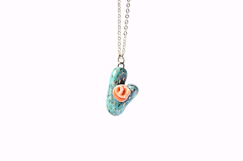 May include: A turquoise ceramic cactus necklace with a pink flower on top. The necklace has a silver chain.
