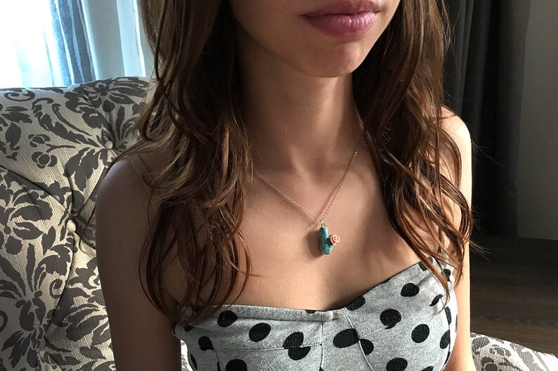 May include: A woman wearing a black and white polka dot top with a silver chain necklace featuring a turquoise and rose gold pendant.