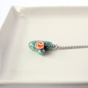 May include: A turquoise and gold heart-shaped pendant with a pink flower on top, hanging from a silver chain.
