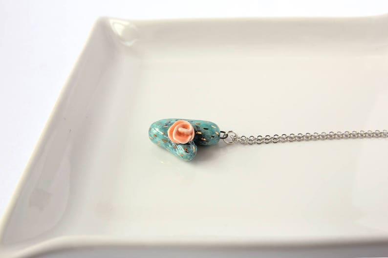 May include: A turquoise and gold heart-shaped pendant with a pink flower on top, hanging from a silver chain.