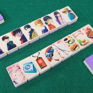 May include: A set of double-sided dominoes with colorful illustrations. One side features anime characters and the other side features Japanese-themed designs like cherry blossoms, fans, and chopsticks.