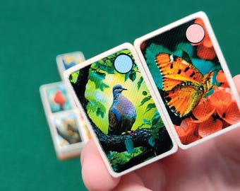 Könnte beinhalten: Zwei Dominosteine mit bunten Bildern. Ein Dominostein zeigt eine blaue und graue Taube, die auf einem Ast mit grünen Blättern sitzt. Der andere Dominostein zeigt einen orangefarbenen Schmetterling mit schwarzen Markierungen auf einer roten Blume.