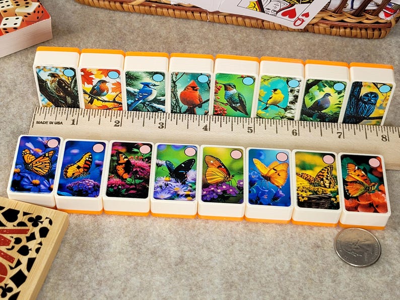 May include: A set of 12 double dominoes with colorful butterfly and bird illustrations. The dominoes are white with orange edges and feature a variety of butterflies and birds, including a cardinal, hummingbird, and blue jay.