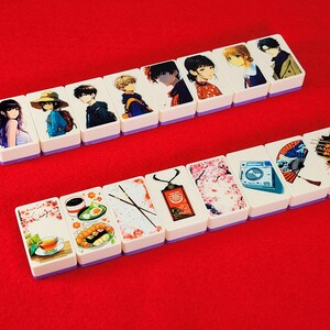 May include: A set of 14 white rectangular tiles with colorful images. The tiles feature anime characters, flowers, food, and other designs. The tiles are arranged in two rows on a red surface.