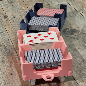 May include: Three-tiered card holder in pink and navy blue, each section filled with playing cards. The pink holder has small wheels. The cards feature red diamond suits and a blue and white pattern.