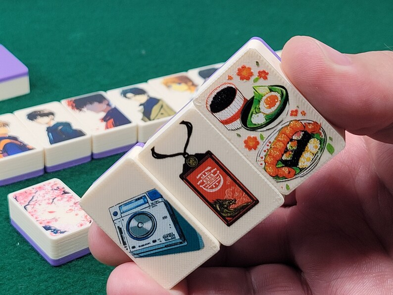 May include: A set of four white dominoes with colorful illustrations. One domino features a camera, another has a necklace with a tag, and the last two have Japanese food illustrations.