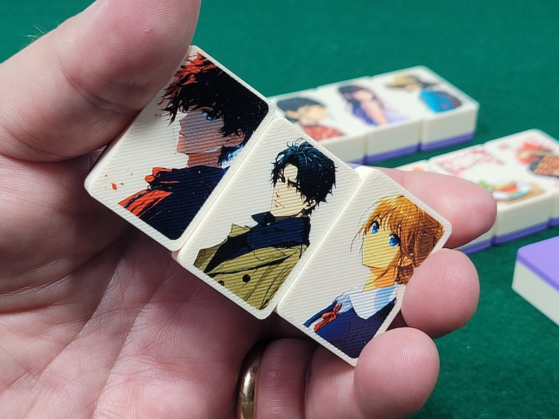 May include: Four white rectangular tiles with colorful anime character illustrations. The tiles are held in a hand. The characters are drawn in a manga style.