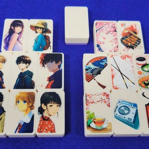 May include: A set of 12 double-sided dominoes with various images, including anime characters, Japanese-inspired designs, and food. The dominoes are white with rounded edges.