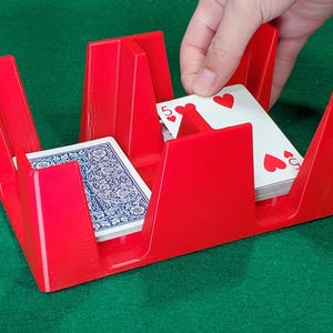 May include: Red plastic card holder with a deck of cards being placed inside. The holder has four slots for cards.