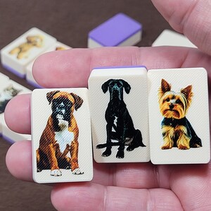 May include: Four white tiles with images of different dog breeds. The tiles are held in a hand. The dogs are a boxer, a Great Dane, a Yorkshire Terrier, and a Labrador Retriever.