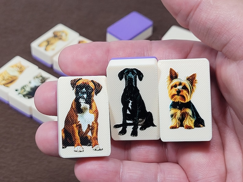 May include: Four white tiles with images of different dog breeds. The tiles are held in a hand. The dogs are a boxer, a Great Dane, a Yorkshire Terrier, and a Labrador Retriever.