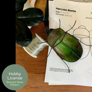 May include: A stained glass pattern for a Hercules Beetle, measuring 12.7 cm by 7 cm. The pattern is printed on white paper and includes instructions for assembling the stained glass project. The skill level is listed as beginner.