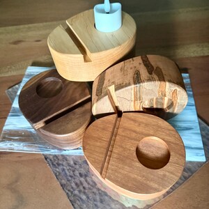 May include: A collection of wooden candle holders in various shapes and wood grains. One holder has a slot for a phone and a small, white LED candle. The other holders have circular cutouts for candles. The wood tones range from light to dark.