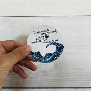 May include: A white round sticker with a blue wave made of hearts. The sticker has the text "If you want to know how much I love you count all the waves in the sea."