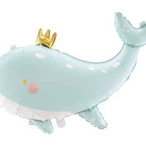 May include: A light blue whale balloon with white polka dots and a gold crown. The balloon is inflated and ready to be used for a party or celebration.