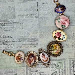 May include: A charm bracelet featuring seven distinct circular and oval links. The links display various colourful floral patterns, a butterfly, and two portrait cameos set in gold-toned metal frames with intricate rope and filigree detailing.