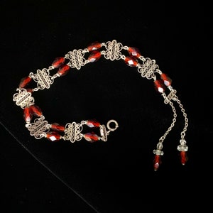 May include: A silver filigree bracelet with red glass beads. The bracelet has a delicate design and is accented with small silver beads.