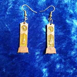 May include: A pair of gold glitter and wood earrings shaped like a grandfather clock.