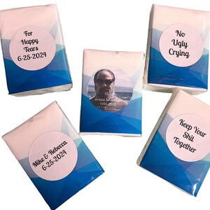 May include: Five tissue boxes with blue and white designs. The boxes have different messages on them, including "For Happy Tears", "No Ugly Crying", "Keep Your Shit Together", and "Mike & Rebecca 6-25-2024". One box has a photo of a man with the text "Arnold Silverman 1956-2013".