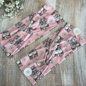 May include: Two pink fabric headbands with a white button on each side. The headbands have a repeating pattern of ghosts, flowers, and the text "Boo Bees" and "Boo Your Boo Bees".