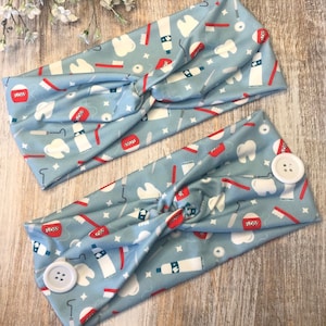 May include: Two blue headbands with a dental theme. The headbands are made of a soft, stretchy fabric and feature a repeating pattern of toothbrushes, toothpaste, floss, and teeth. The headbands have a button on each side for added functionality.