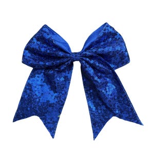 May include: A large, royal blue hair bow. The bow is covered in sequins, giving it a sparkly appearance. The bow is tied in the center with long, pointed tails. This accessory is suitable for cheerleading or dance.