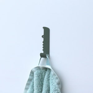 A bathroom wall hook with the shape of a crocodile, seen from the side and facing right. It is made out of stainless steel and painted with a green color. The crocodile´s body has been bent up in to one hook, to put backpacks, jackets and keys on.