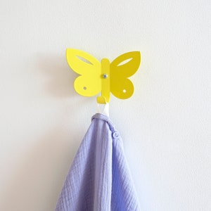 A animal wall hook with the shape of a butterfly. It is made out of steel and painted with a yellow color. The butterfly´s body has been bent up in to one hook, to put backpacks, jackets and keys on.
