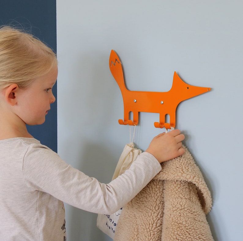 A animal wall hook with the shape of a fox, seen from the side and facing right. It is made out of steel and painted with a grey color. The fox´s legs has been bent up in to four individual hooks to put backpacks, jackets and keys on.