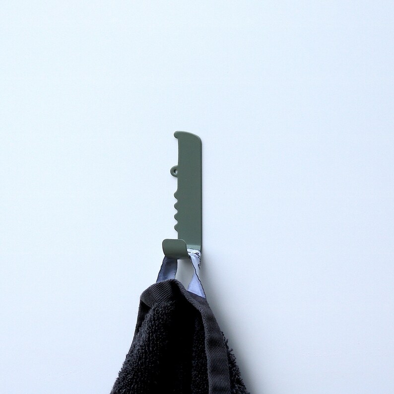 A bathroom wall hook with the shape of a crocodile, seen from the side and facing right. It is made out of stainless steel and painted with a green color. The crocodile´s body has been bent up in to one hook, to put backpacks, jackets and keys on.