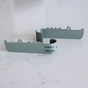 A bathroom wall hook with the shape of a crocodile, seen from the side and facing right. It is made out of stainless steel and painted with a green color. The crocodile´s body has been bent up in to one hook, to put backpacks, jackets and keys on.