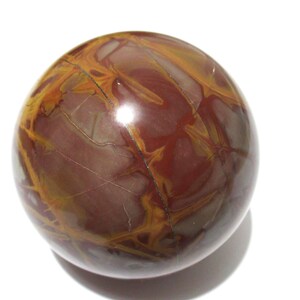 May include: A polished, spherical gemstone with a rich, earthy color palette. The orb features a deep burgundy base, interwoven with striking veins of golden-yellow and lighter brown hues. The surface is smooth and reflective, showcasing natural patterns.