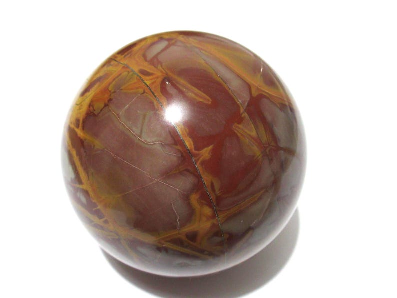 May include: A polished, spherical gemstone with a rich, earthy color palette. The orb features a deep burgundy base, interwoven with striking veins of golden-yellow and lighter brown hues. The surface is smooth and reflective, showcasing natural patterns.