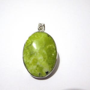 May include: Oval-shaped pendant with a bright green stone, set in a silver-colored metal frame. The stone has a marbled appearance with lighter green and white inclusions. The pendant has a small loop at the top for a chain.