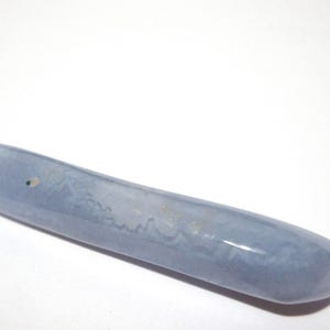 May include: A smooth, elongated, light blue stone with a rounded shape. The stone has subtle variations in color and texture, and appears to be polished. The object is set against a white background.