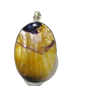 Puede incluir: Colgante ovalado con una fianza plateada. El colgante presenta una piedra pulida con un degradado de color amarillo, morado y blanco. La piedra tiene una grieta que atraviesa el centro.