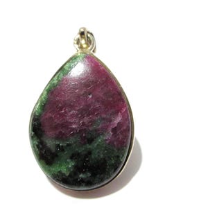 May include: A teardrop-shaped pendant featuring a polished ruby and zoisite stone with deep magenta, dark green, and black mottled patterns, encased in a simple silver-toned metal setting with a small circular bail at the top for attachment.